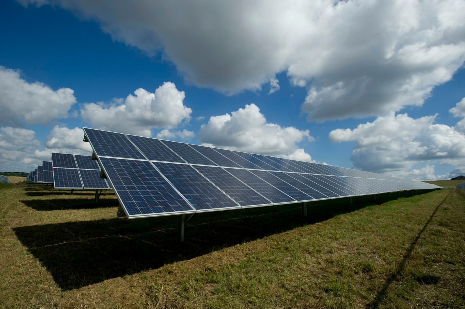 Ground-mounted solar panel rows under a partly cloudy sky