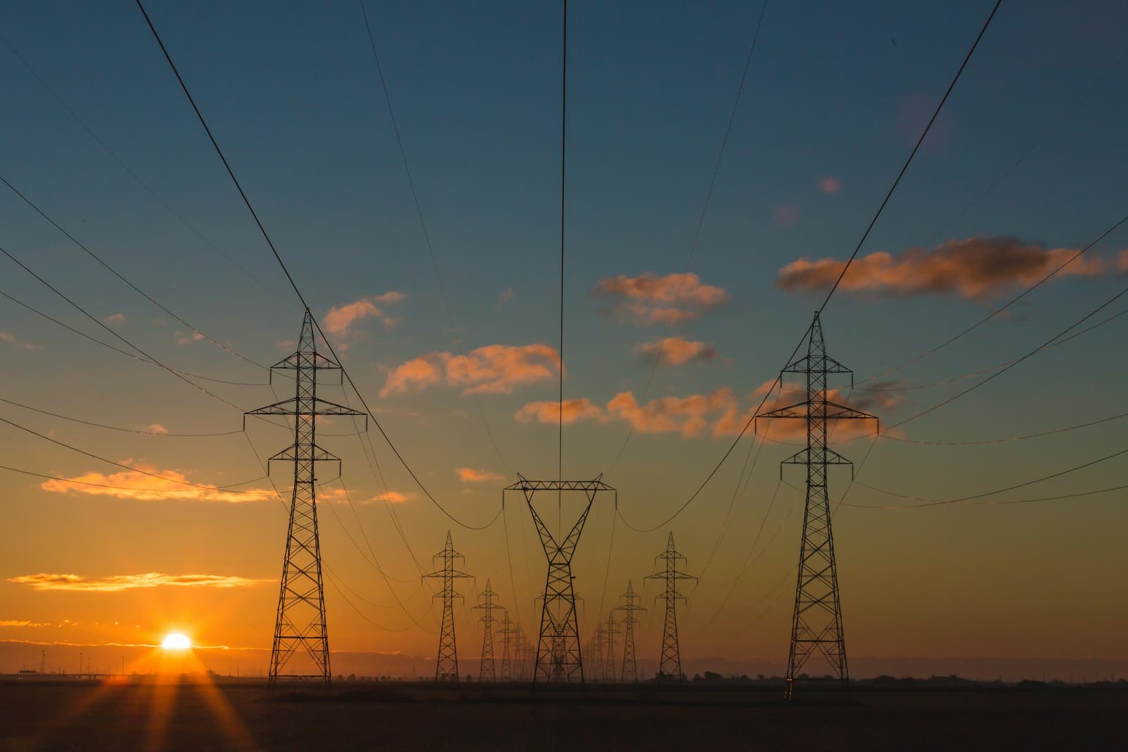 High-voltage transmission towers silhouetted against a sunset